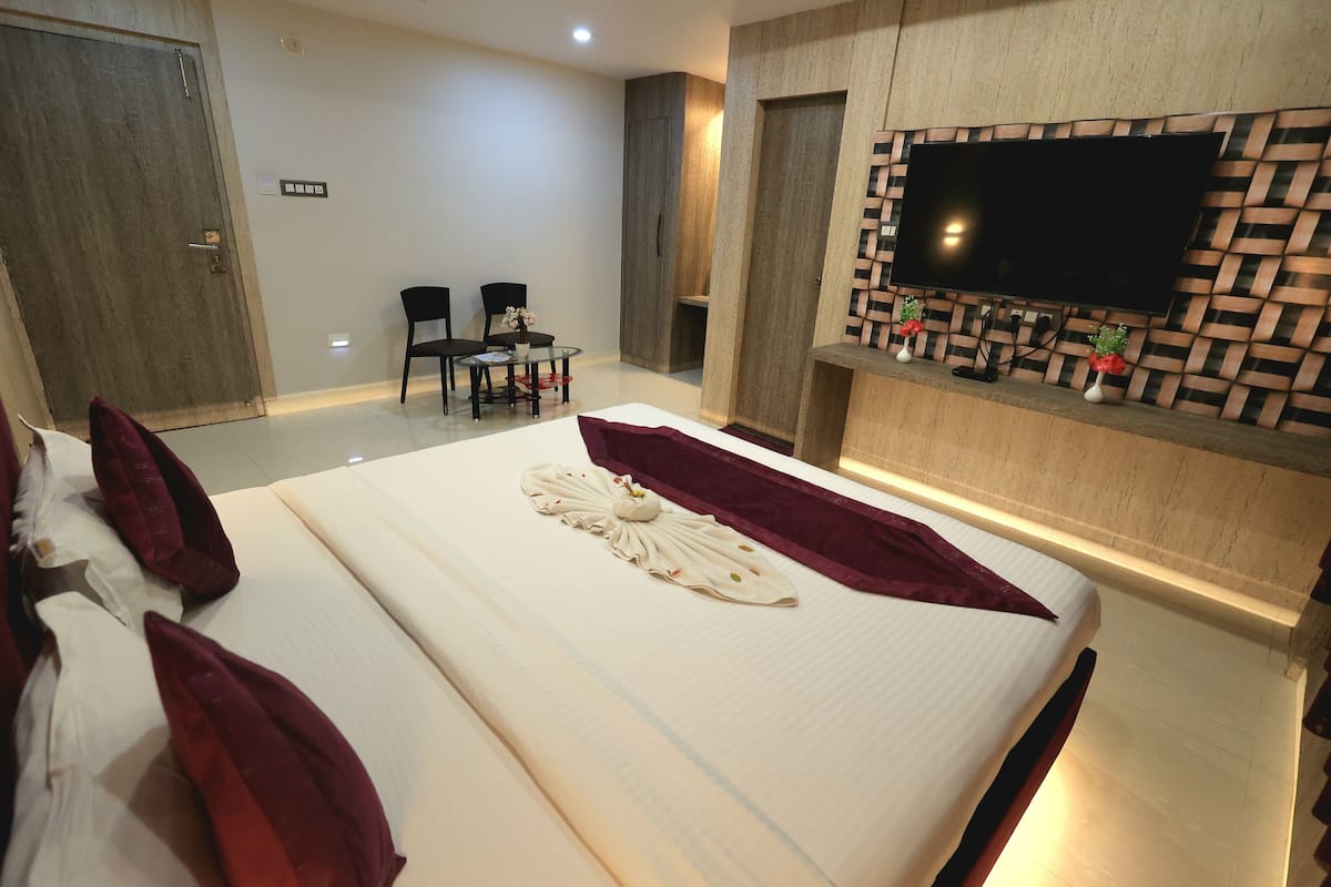 Une chambre d’hôtel avec un grand lit, un téléviseur à écran plat fixé à un mur en bois, une petite table avec des chaises et une armoire en bois.