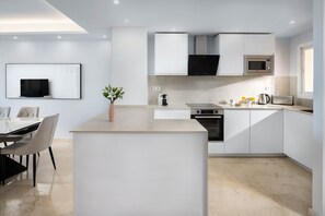 Une cuisine moderne avec des meubles blancs, un îlot central, un four à micro-ondes, un four traditionnel et un coin repas avec une table et des chaises.