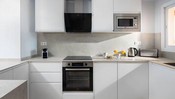 A modern kitchen with white cabinetry, a built-in oven, a microwave, a toaster, and a coffee maker.