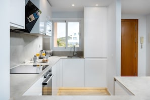 Cozinha moderna com armários brancos, forno embutido e janela com vista para edifícios.