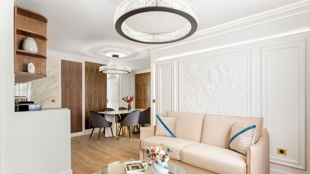 Ein modernes Wohnzimmer mit einem beigefarbenen Sofa, einem Glastisch und einem Essbereich mit weißem Tisch und Stühlen.