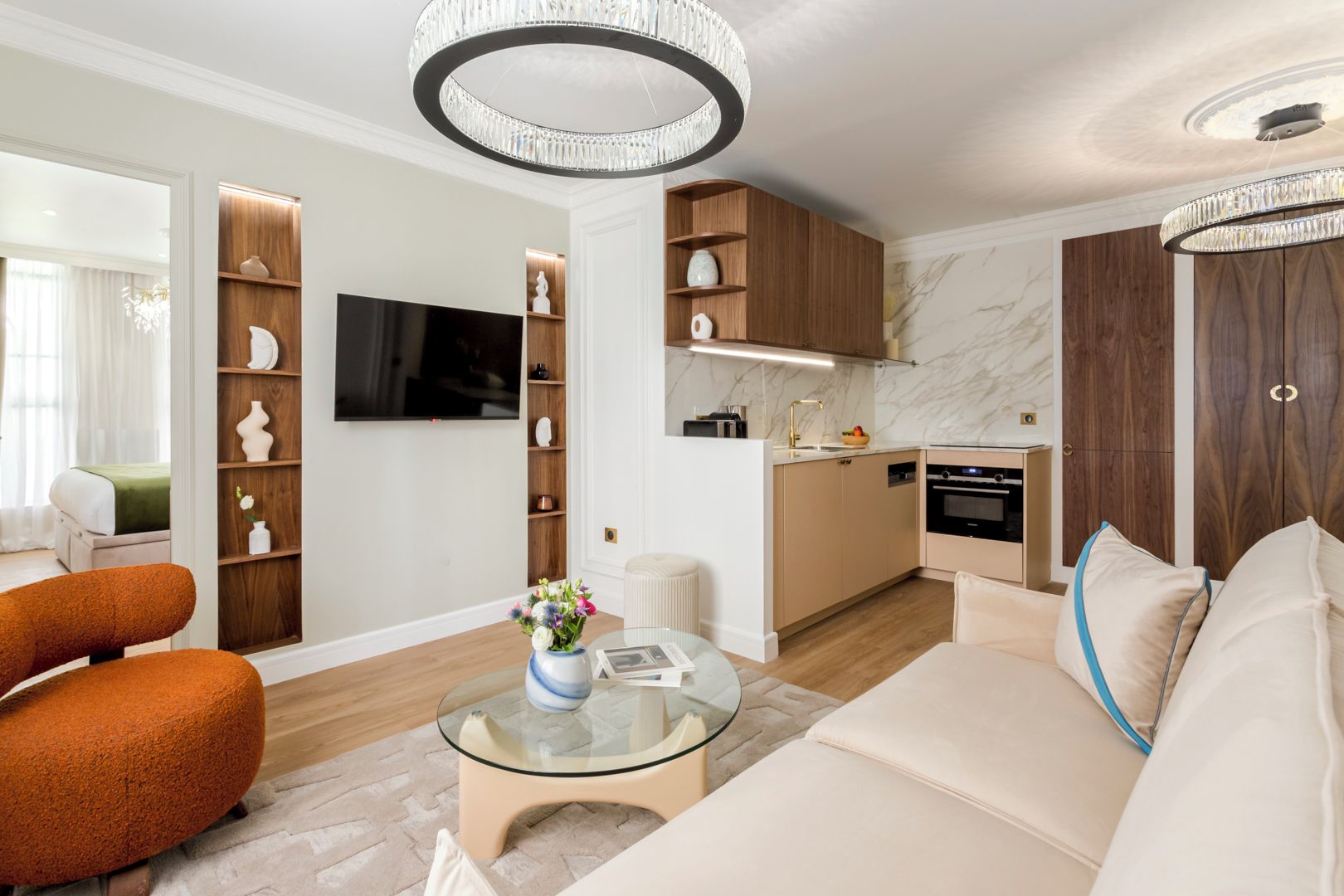 Ein modernes Wohnzimmer mit einer Couch, einem Glastisch und einem Fernseher. Es gibt eine Küchenzeile mit Holzschränken und einer Marmor-Spritzschutzleiste.