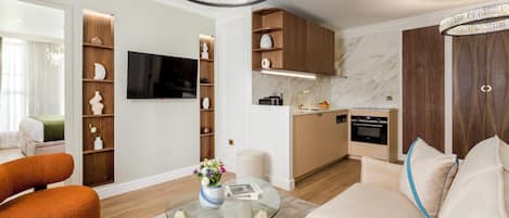 Ein modernes Wohnzimmer mit einer Couch, einem Glastisch und einem Fernseher. Es gibt eine Küchenzeile mit Holzschränken und einer Marmor-Spritzschutzleiste.