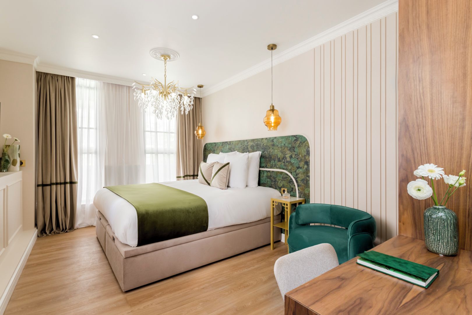 A modern hotel room with a large bed, a desk, a chair, a chandelier, and a wooden panel wall.