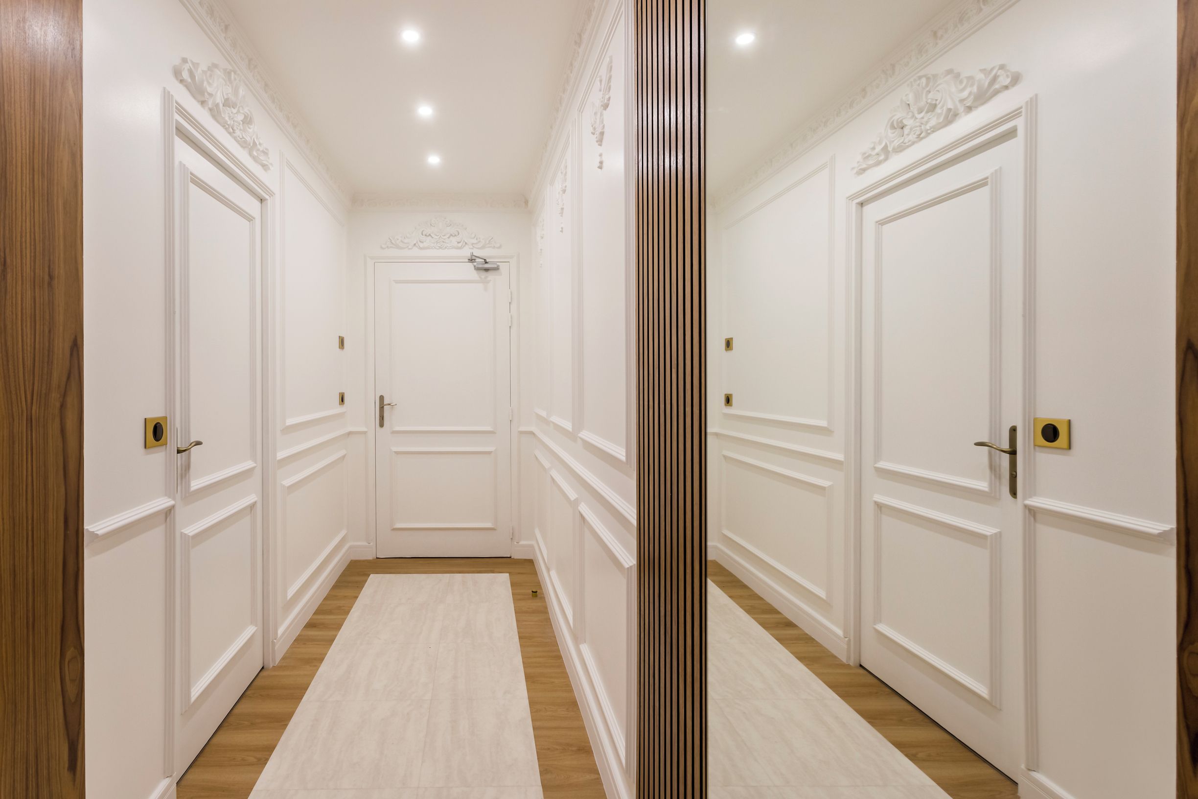 A hallway with white doors, wooden flooring, and a central column.