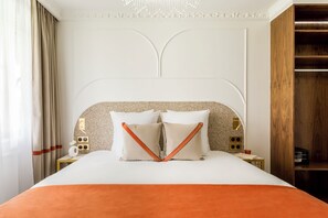Ein ordentlich bezogenes Bett mit einer weiß-orangenen Tagesdecke, zwei weiße Kissen und ein Nachttisch aus Holz mit einer Lampe und einem kleinen Tisch mit einem Buch und einer Tasse.