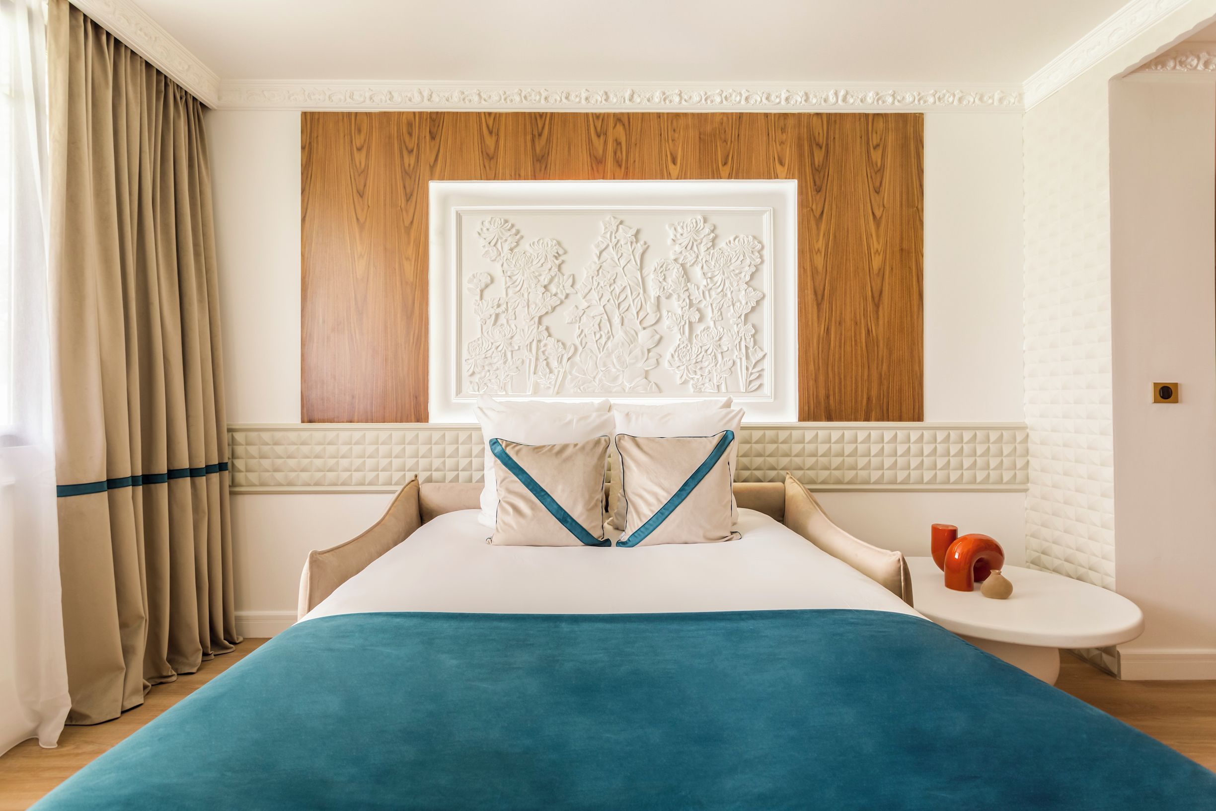 Una habitación de hotel con una cama, una mesita de noche, una ventana con cortinas y una obra de arte colgada en la pared.