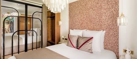A hotel room with a large bed, a chandelier, a floral-patterned wall, and a sliding door leading to a bathroom.