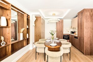A modern dining area with a round table, beige upholstered chairs, and a vase of flowers.