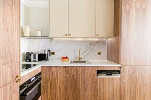 A compact kitchen with wooden cabinetry, a marble countertop, a built-in oven, a coffee maker, a toaster, and a fruit bowl. - Merveil - Luxury Suite - Marais - Lenoir III (Paris)