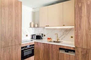 Eine kleine Küche mit Holdekor-Schränken, einer Marmorarbeitsplatte, einem eingebauten Backofen, einer Kaffeemaschine, einem Toaster und einem Spülbecken mit goldenem Wasserhahn.