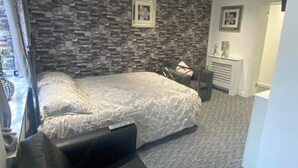 A bedroom with a stone-patterned wall, a bed with a white bedspread, a black chair, and a fireplace.