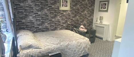 A bedroom with a stone-patterned wall, a bed with a white bedspread, a black chair, and a fireplace.
