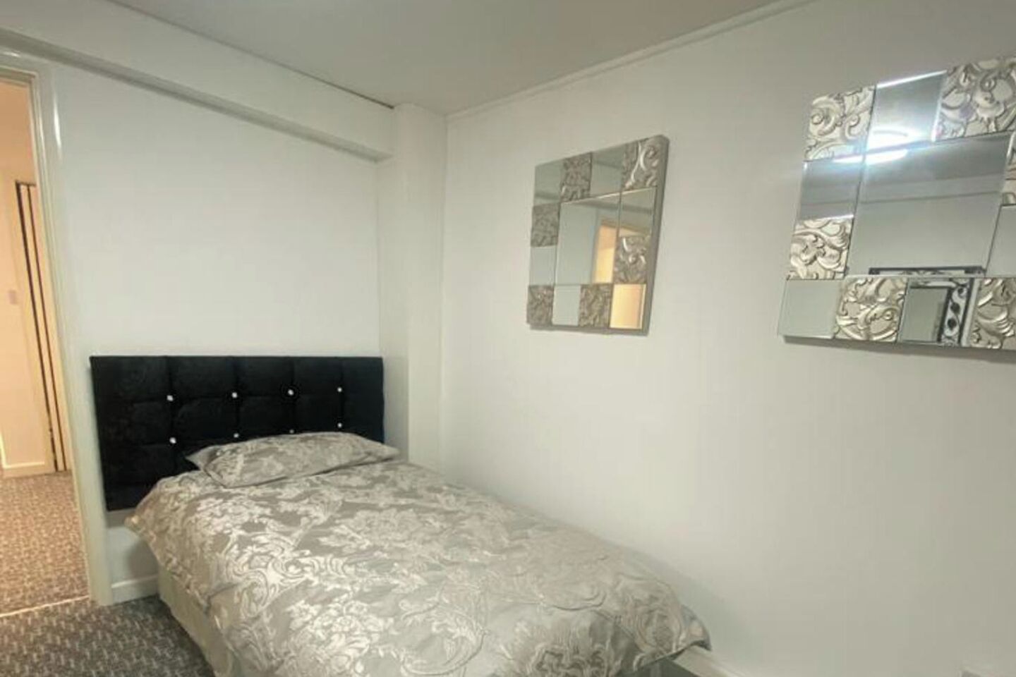 A bedroom with a bed, a door, and a wall-mounted mirror.