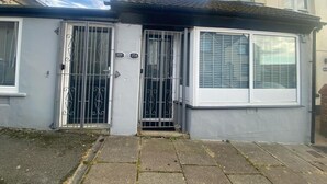 A two-story residential building with a grey exterior, a gated front door, and a window with blinds.