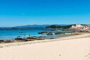 Una playa con barcos, costa rocosa y edificios al fondo.