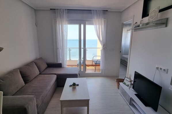 Una sala de estar moderna con un sofá, una mesa de centro, un televisor y un balcón con vistas al mar.