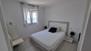 Une chambre à coucher avec un lit, des tables de chevet, un banc et une fenêtre avec des rideaux.