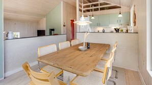Una cocina moderna con armarios blancos, una mesa de comedor de madera con sillas e iluminación colgante.