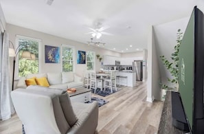 A modern living room with a sofa, dining table, and kitchen in the background.