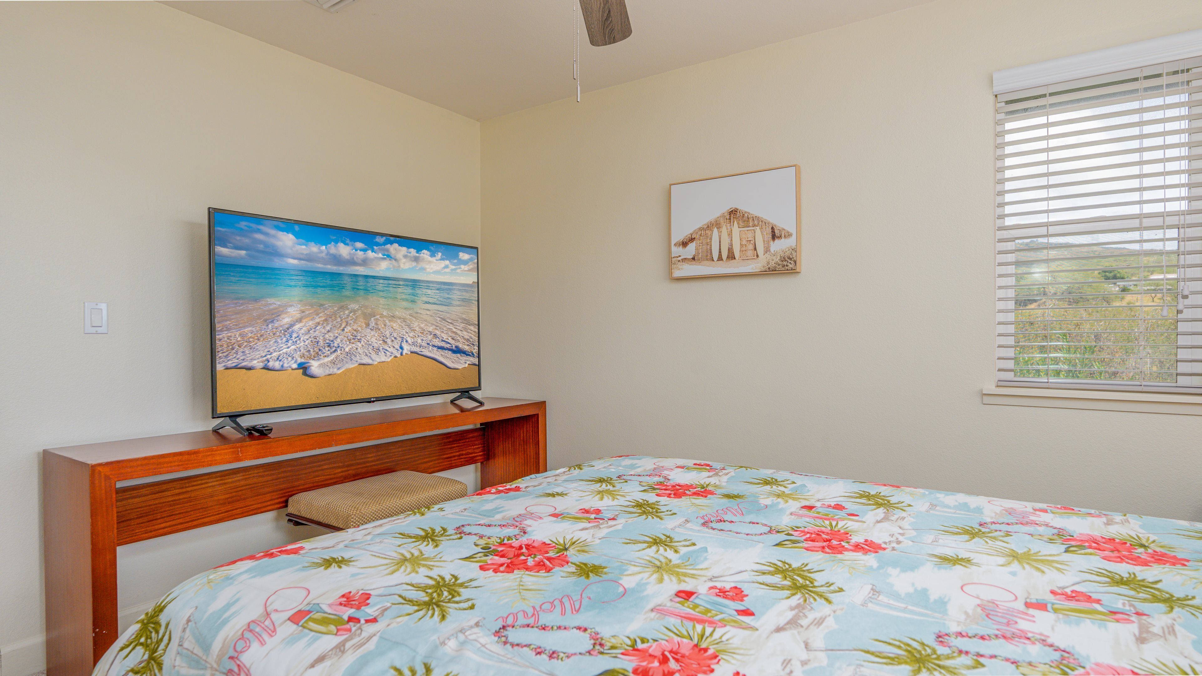 A bedroom with a bed, a TV on a wooden stand, a framed picture on the wall, and a window with blinds.