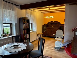 A dining area with a table, chairs, a bookshelf, a radiator, and a window with curtains.