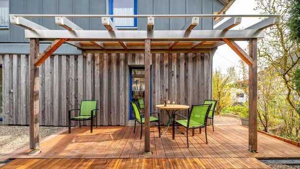 A covered outdoor seating area with a wooden deck, green chairs, and a round table. - Apartment 'Ferienwohnung Karleidoskope' with Private Terrace, Private Garden and Wi-Fi (Buhlenberg)