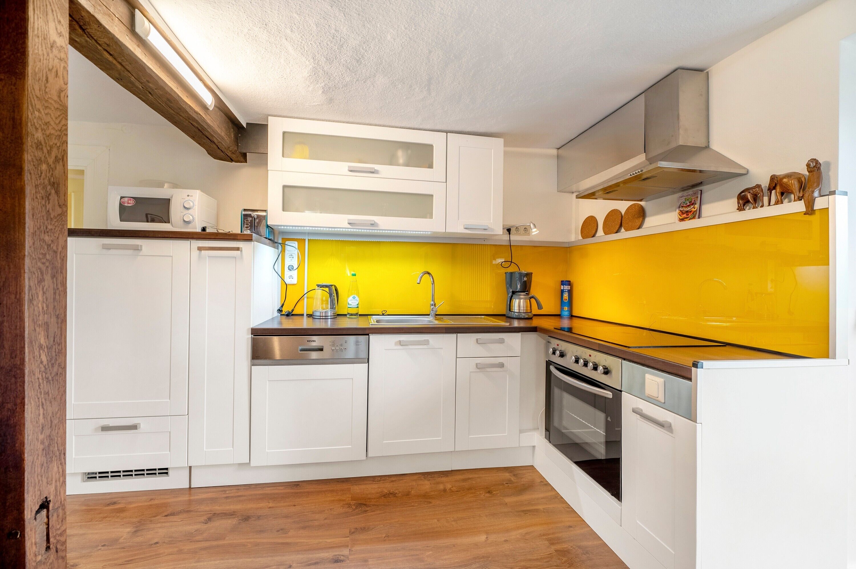 A compact kitchen with white cabinets, a yellow backsplash, a stainless steel stove, and a microwave.
