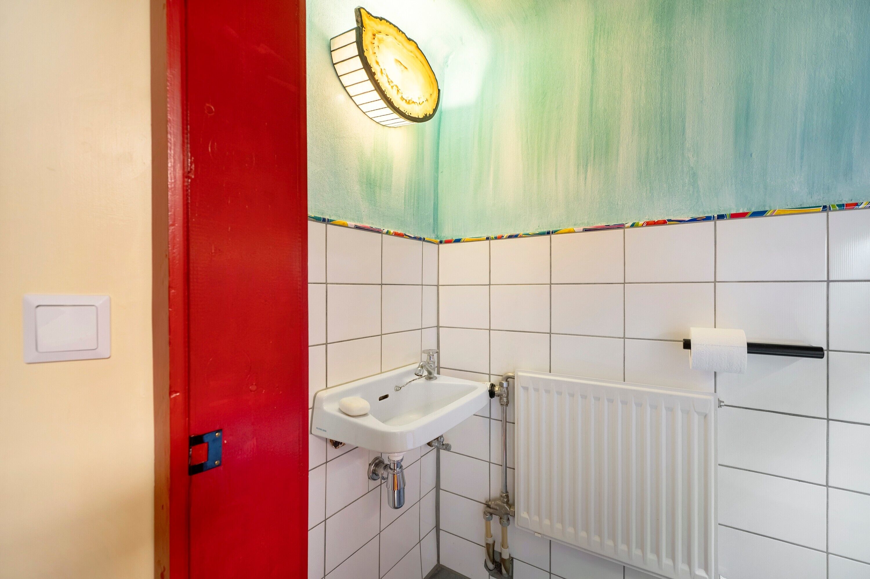 A bathroom with a white sink, a red door, and a white radiator.