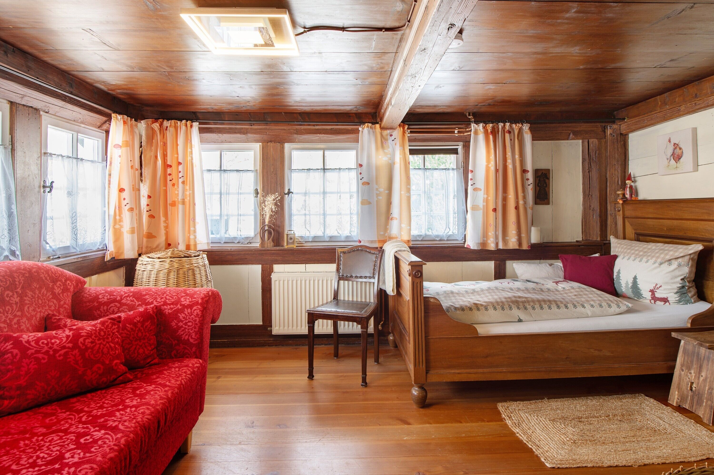 Een houten kamer met een bed, een rode bank en een stoel.