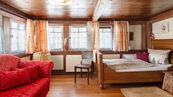 Ein Zimmer mit Holzboden, einem Bett, einer roten Couch und einem Sessel.