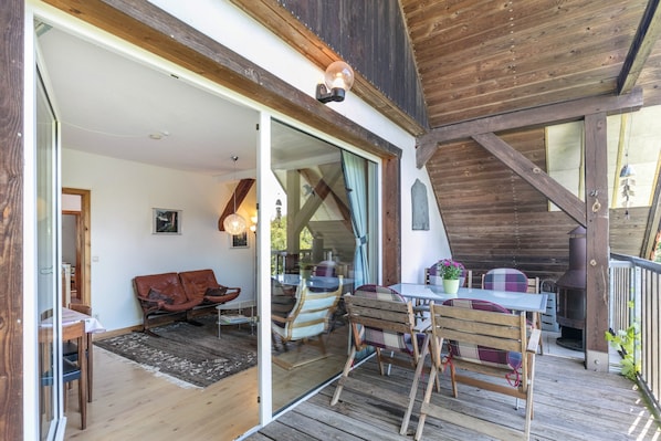 A wooden deck with a table and chairs, a sofa, and a fireplace.