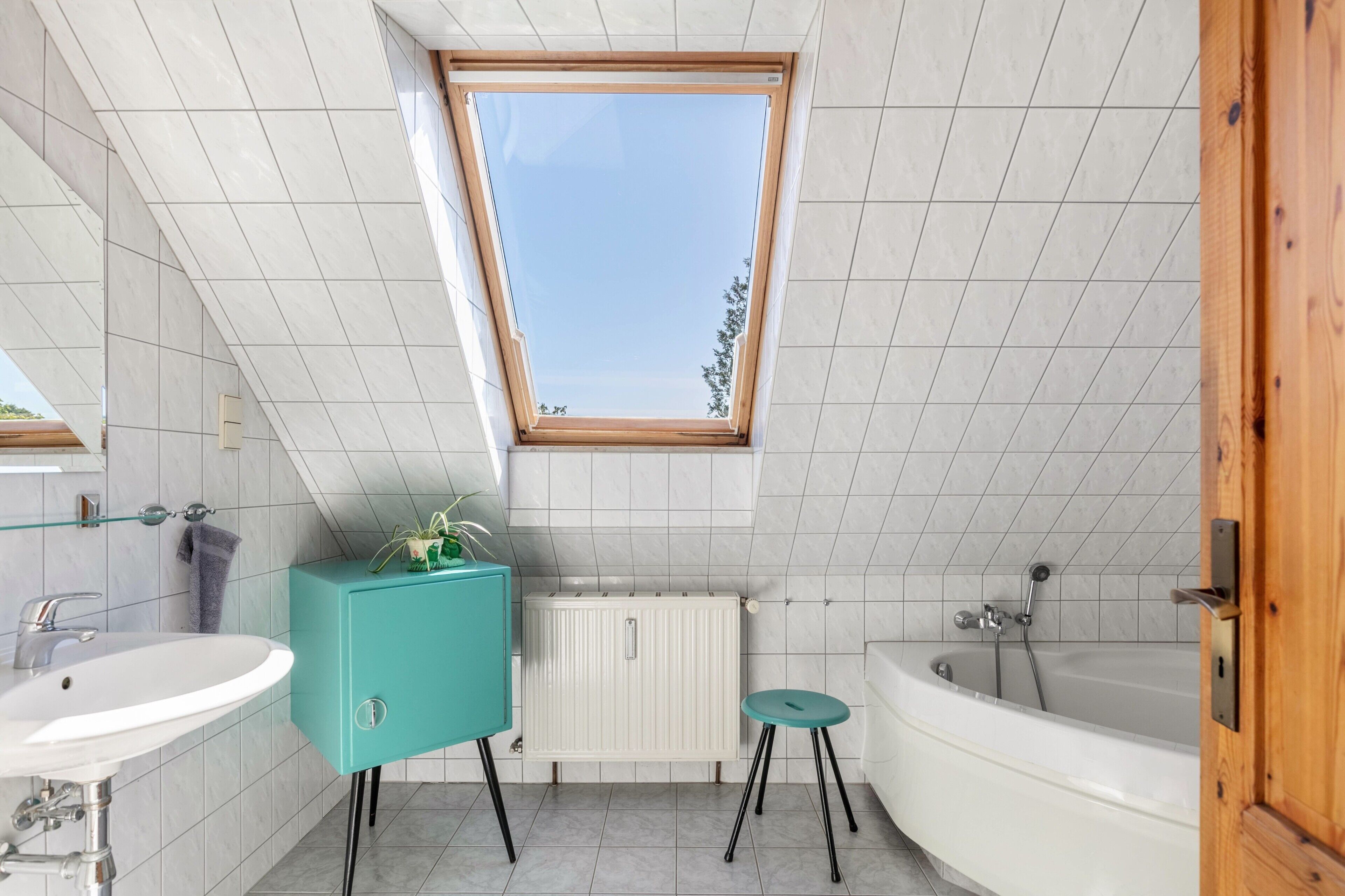 A modern bathroom with a skylight, white tiles, a turquoise cabinet, a white sink, and a bathtub.