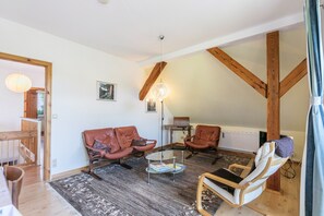 A living room with a wooden ceiling, leather chairs, a glass coffee table, and a patterned rug.