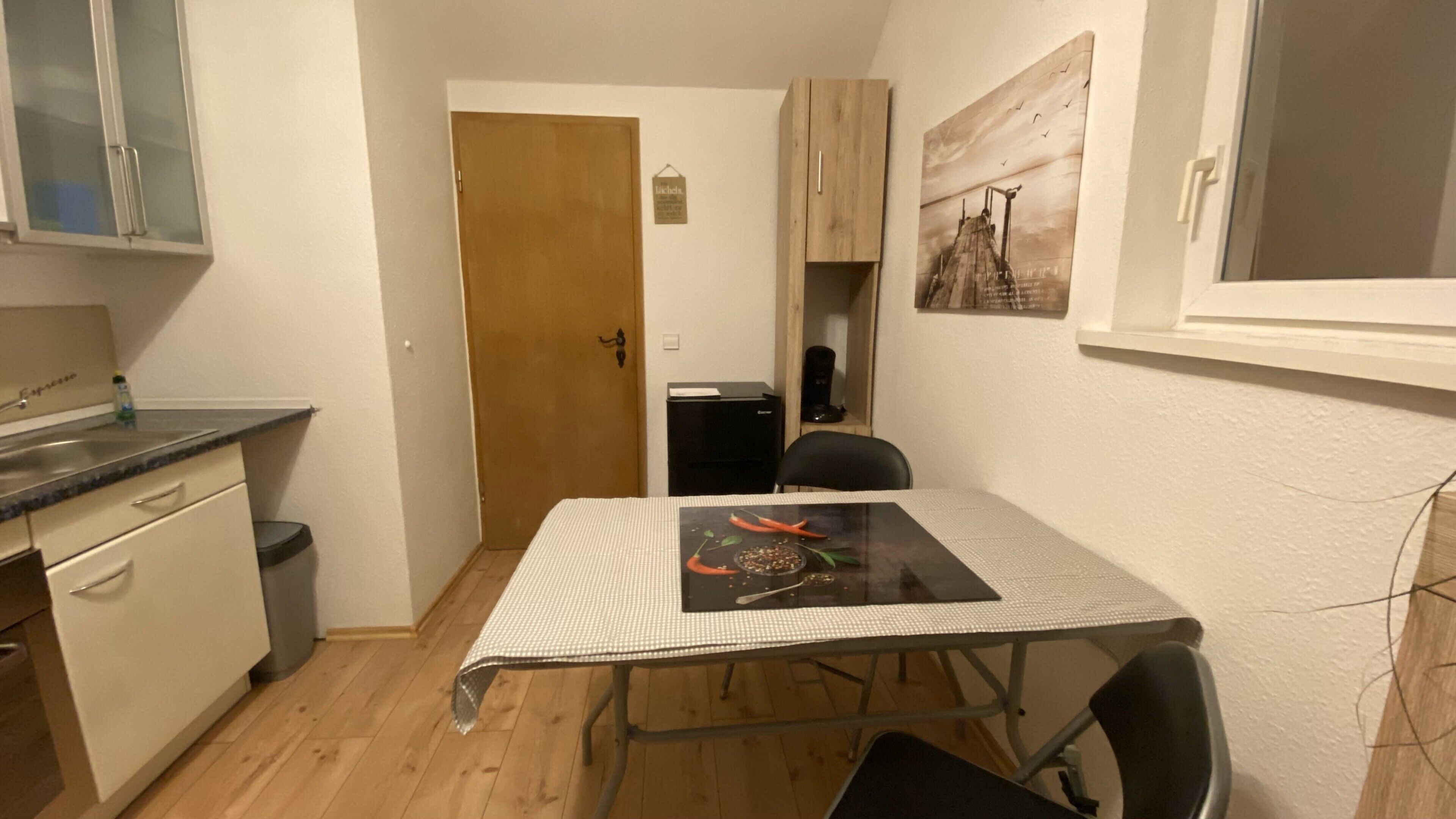 Une cuisine de taille réduite comprenant une table à manger, un réfrigérateur et une porte donnant sur une autre pièce.