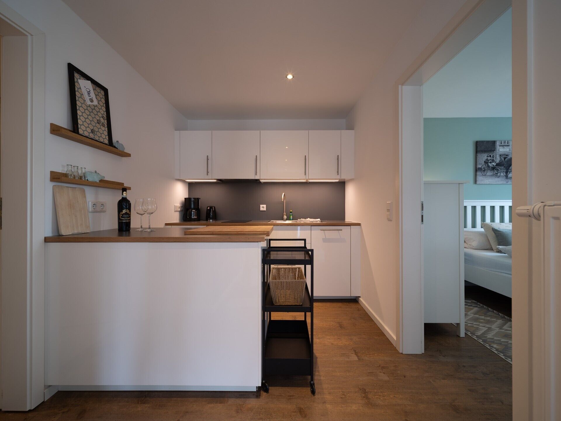 A modern kitchen with white cabinets, a wooden countertop, and a small island. There is a dining area with a bench and a basket.