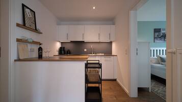 A modern kitchen with white cabinets, a wooden countertop, and a small island. There is a dining area with a bench and a basket.