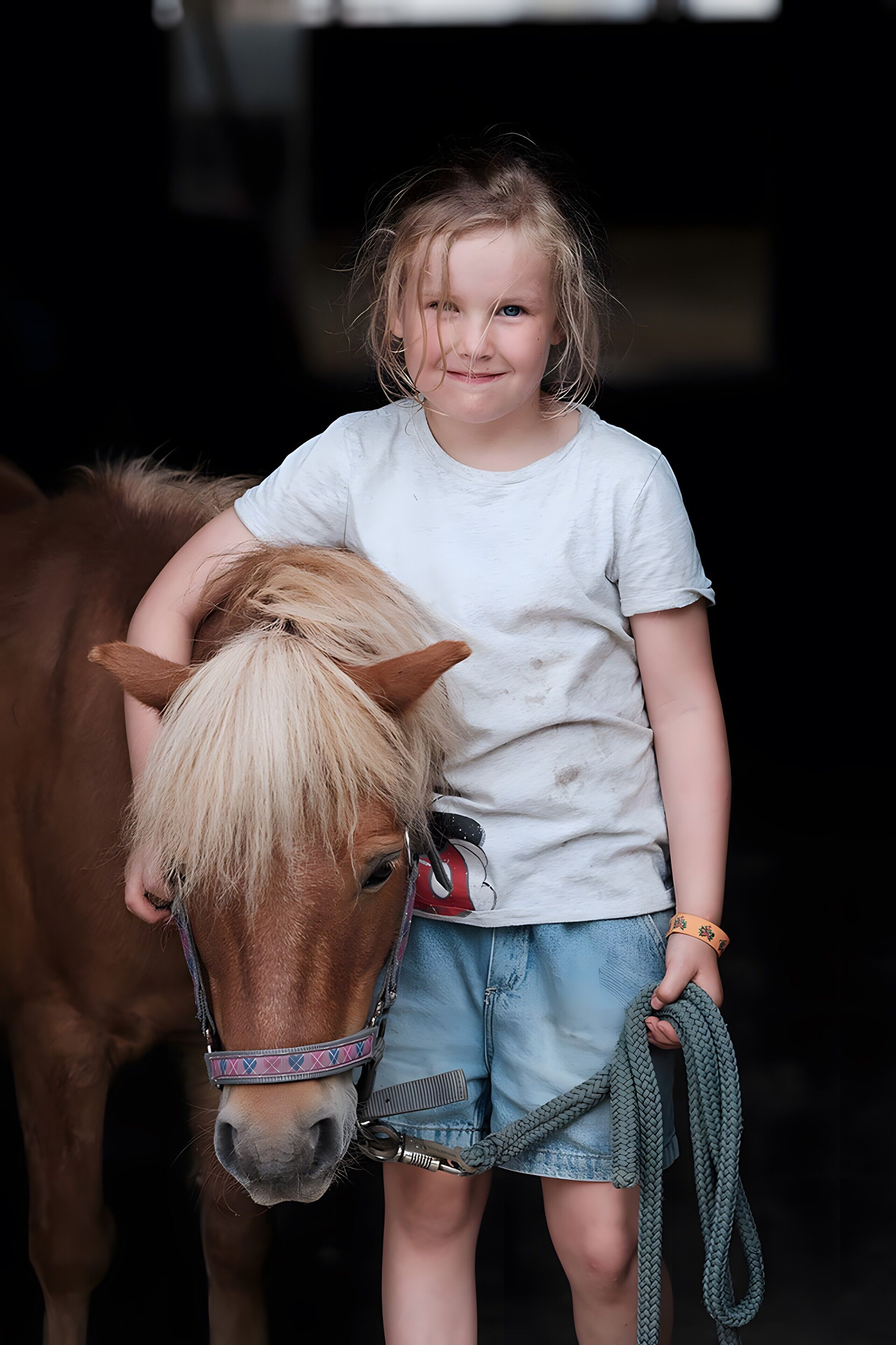 Criança ao lado de um cavalo, segurando uma corda.