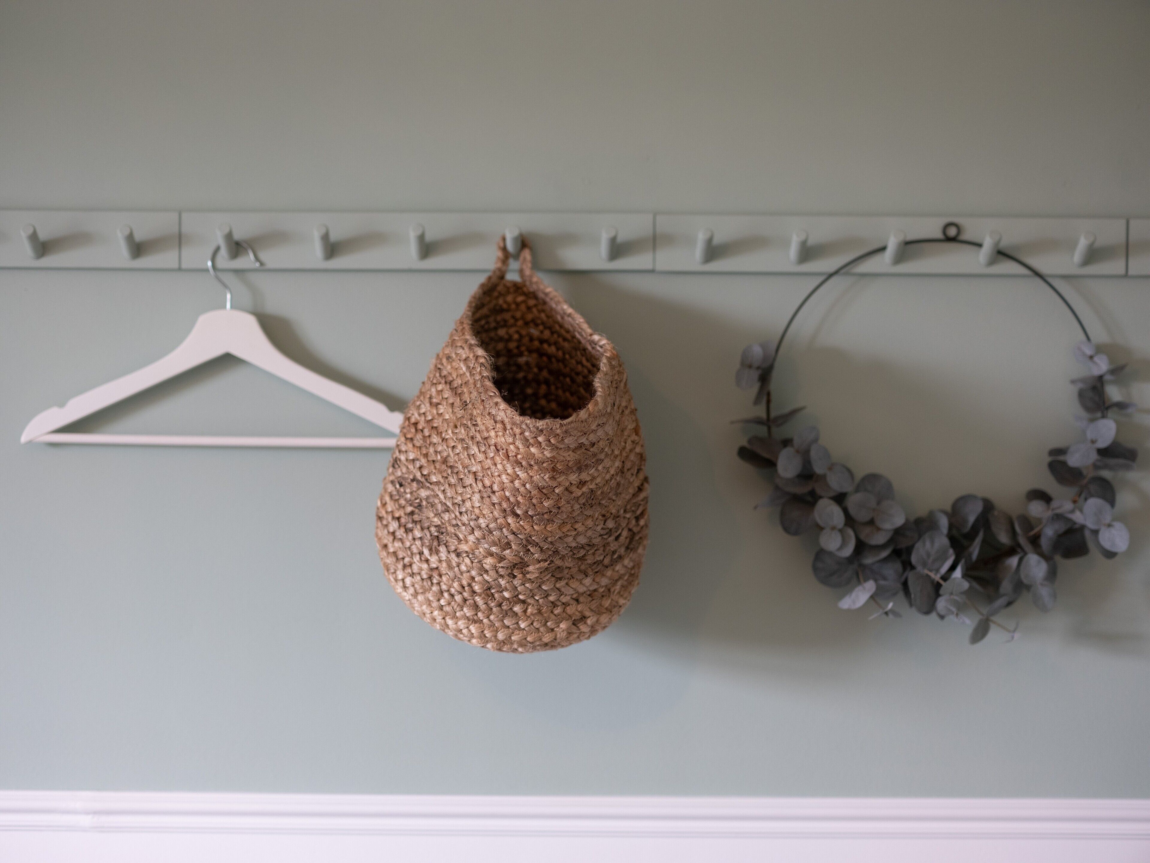 Un gancho de pared con una cesta tejida y una corona decorativa.