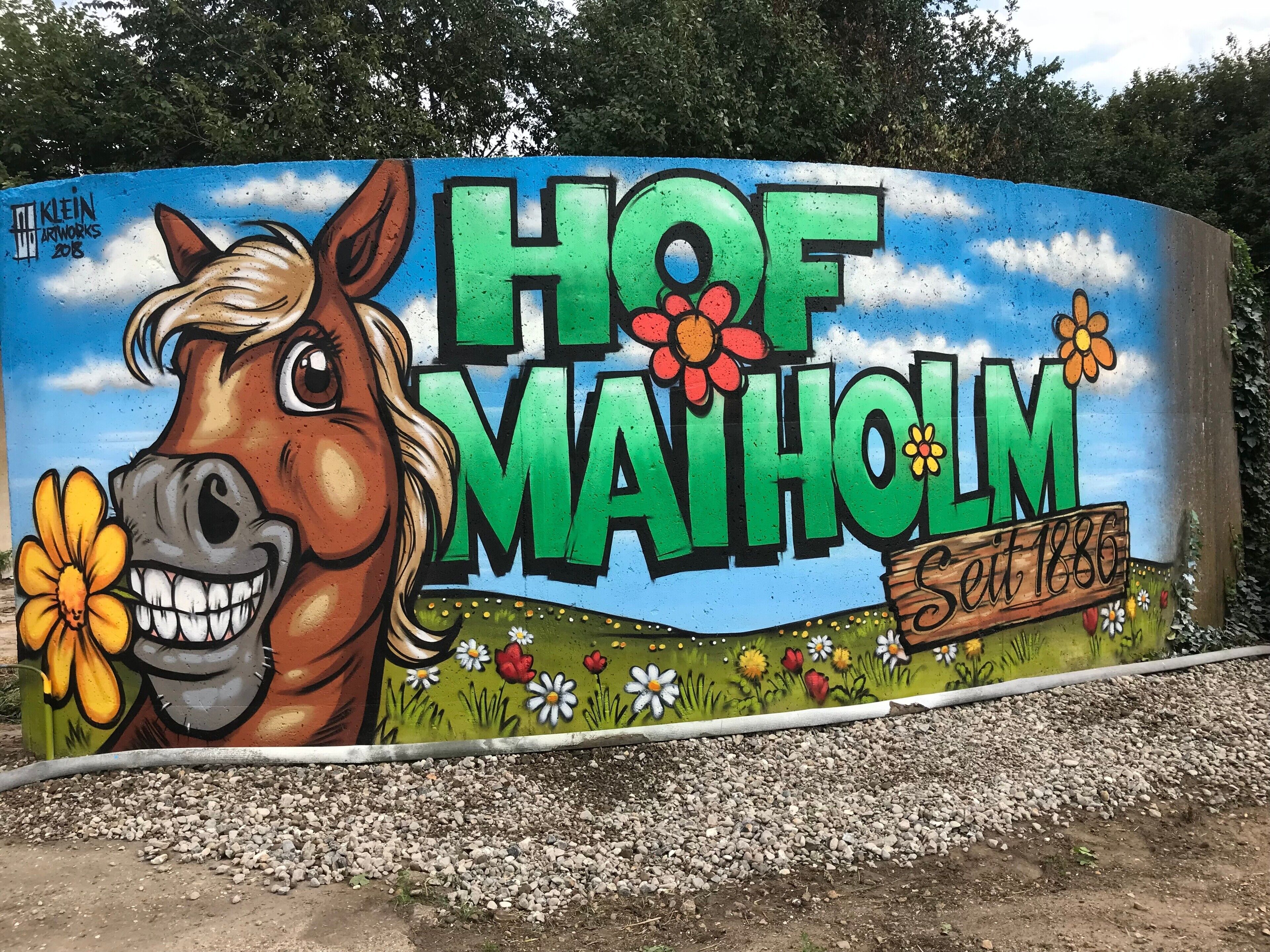 Une fresque représentant un cheval et des fleurs, avec l’inscription « HOF MAIHOLM Depuis 1886 » sur un mur incurvé.