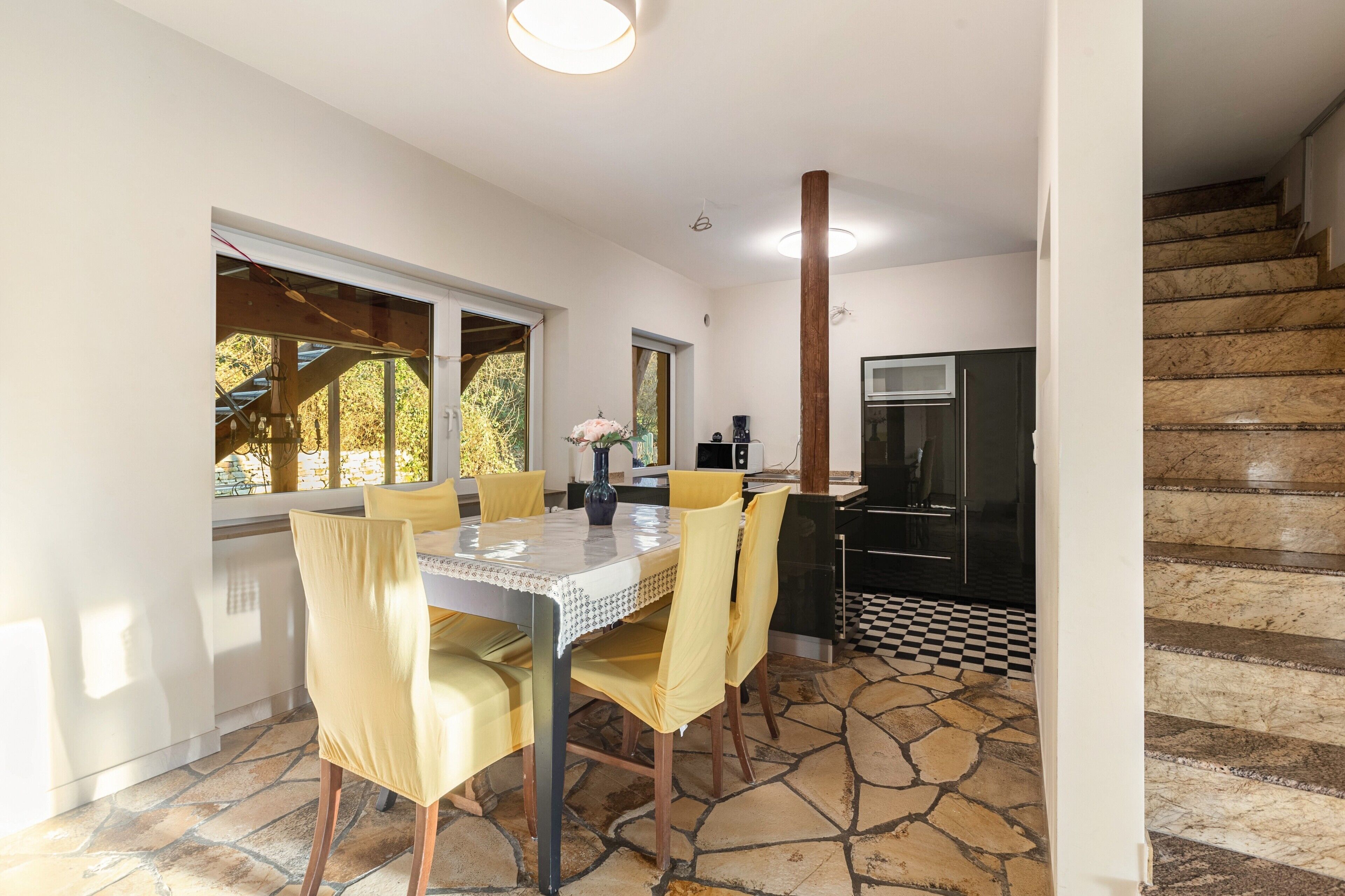 Un coin repas avec une table et des chaises, une cuisine avec un réfrigérateur noir et un escalier avec un sol à carreaux.