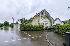 A residential building with a balcony, a car parked in front, and a paved road with directional arrows. - Sunny Apartment with Balcony and Wi-Fi (Küssaberg)
