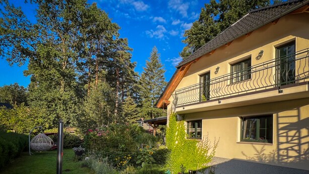 Een twee verdiepingen tellend huis met een balkon, omringd door een tuin met diverse planten en een schommel.