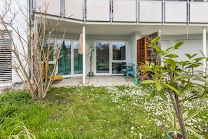 Un edificio moderno con un porche cubierto, puertas de cristal y un jardín de flores blancas.