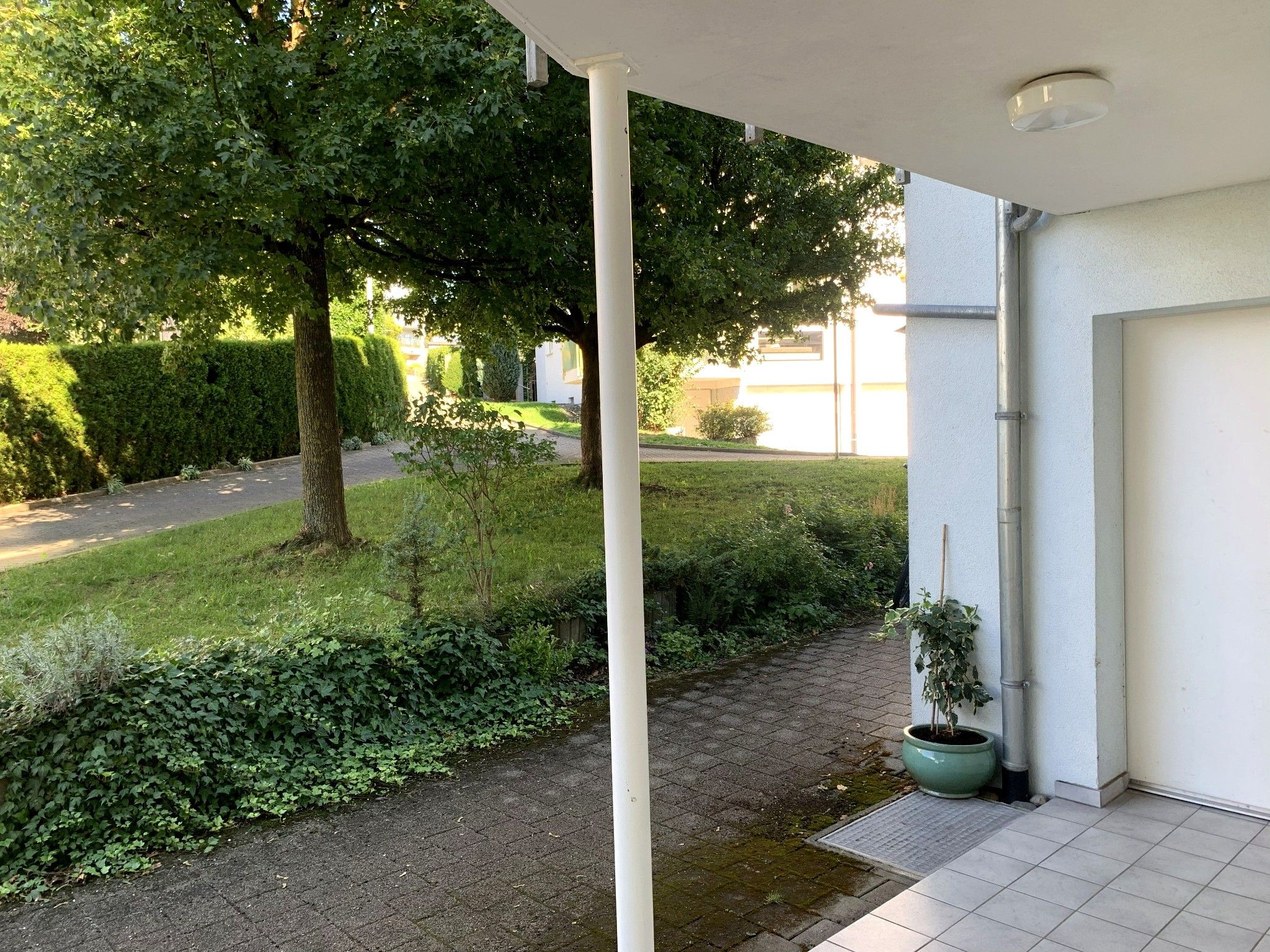 Un espace extérieur abrité, doté d’un chemin pavé, d’un pot de fleurs et d’une colonne blanche.