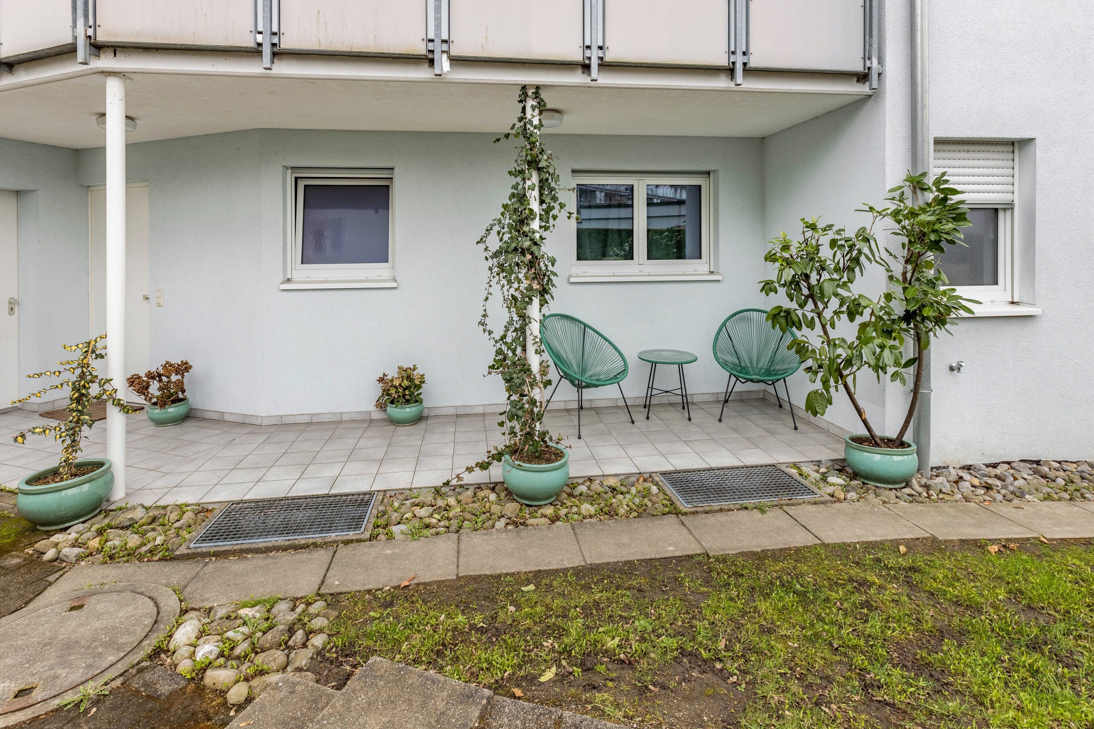 Ein Gebäude mit überdachter Terrasse, Blumentöpfen und Sitzgelegenheiten im Freien.