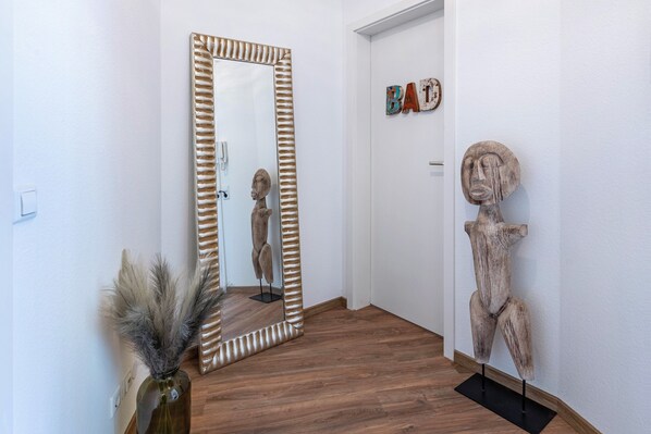 Een gang met een houten vloer, een spiegel met een gestreepte lijst en een beeld aan de muur.