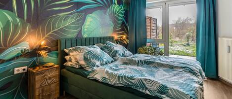 Ein Schlafzimmer mit einem großen Bett, einem Nachttisch, einem Wandbild und einem Fenster mit Vorhängen.
