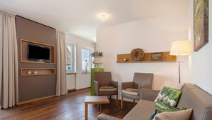 A modern living room with a flat-screen TV, two armchairs, a sofa, a small table, and a lamp. - Obst- und Ferienhof Lehle – Apartment Jonagold with Shared Terrace, Garden & Wi-Fi (Immenstaad am Bodensee)