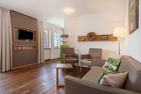A modern living room with a flat-screen TV, two armchairs, a sofa, a small table, and a lamp.